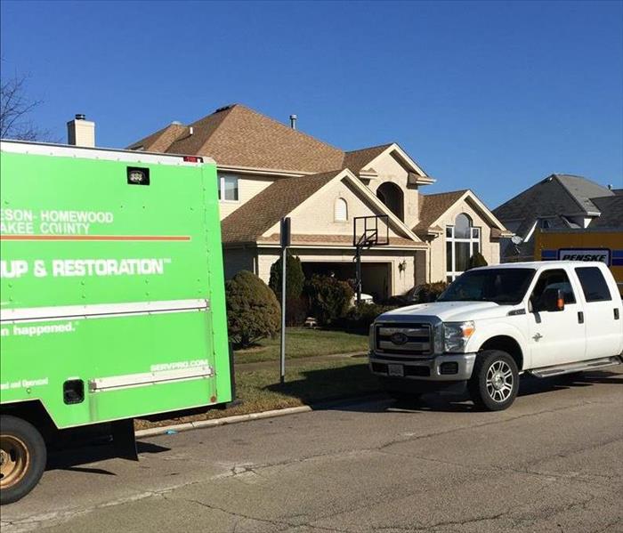 SERVPRO truck and white truck outside of a large brown house with a basketball net
