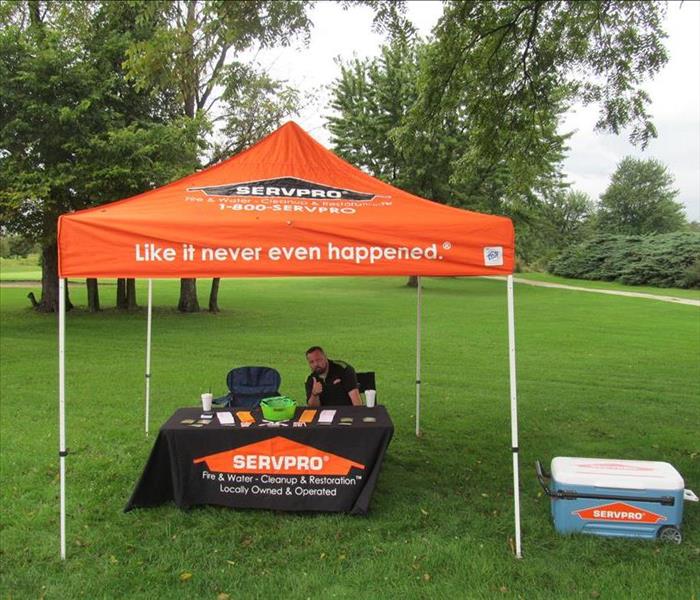 Male SERVPRO representative at golf outing underneath an orange SERVPRO tent