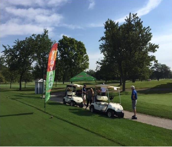 Two golf carts and a SERVPRO banner with three SERVPRO representatives standing nearby at a golf course.